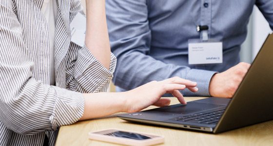 Detailaufnahme eines Laptops an dem zwei InfoFabrik Mitarbeiter gemeinsam arbeiten.
